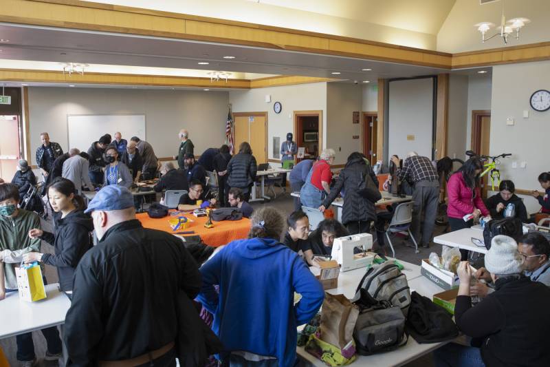 A large room filled with groups of people clustered in groups around tables.