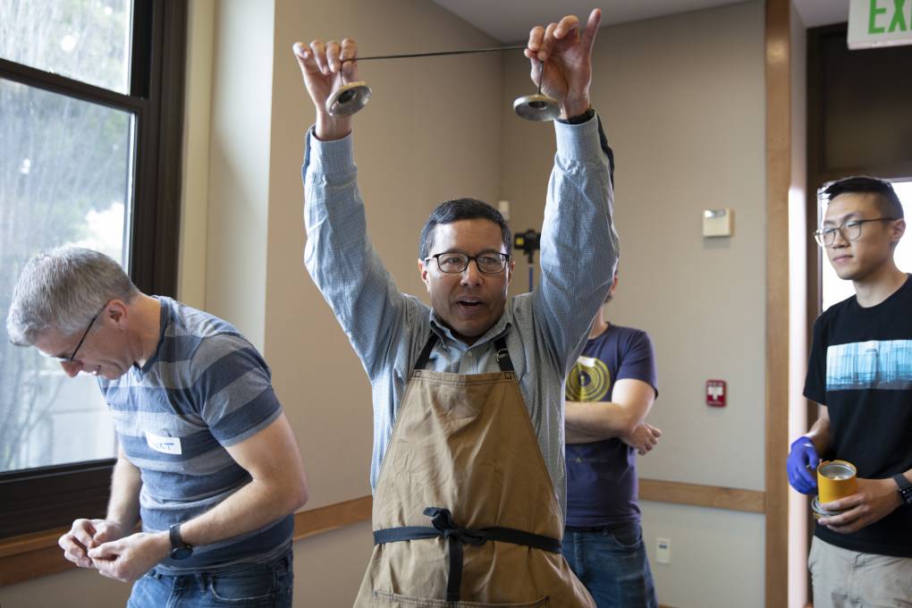 A person wearing a work apron holds up a set of bells in an indoor setting.
