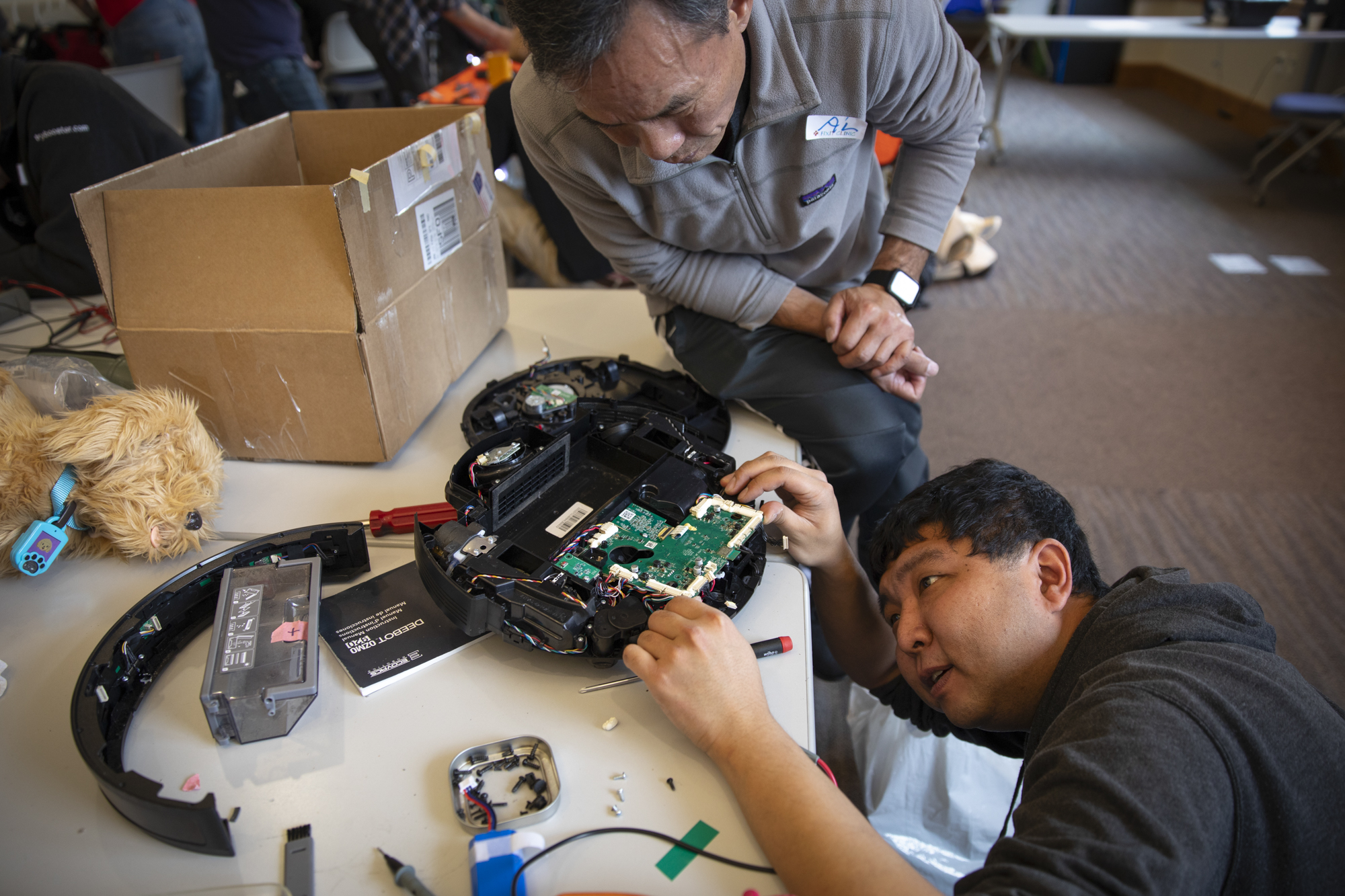 Two people look at the circuit boar inside a disk-shaped device in an indoor setting.