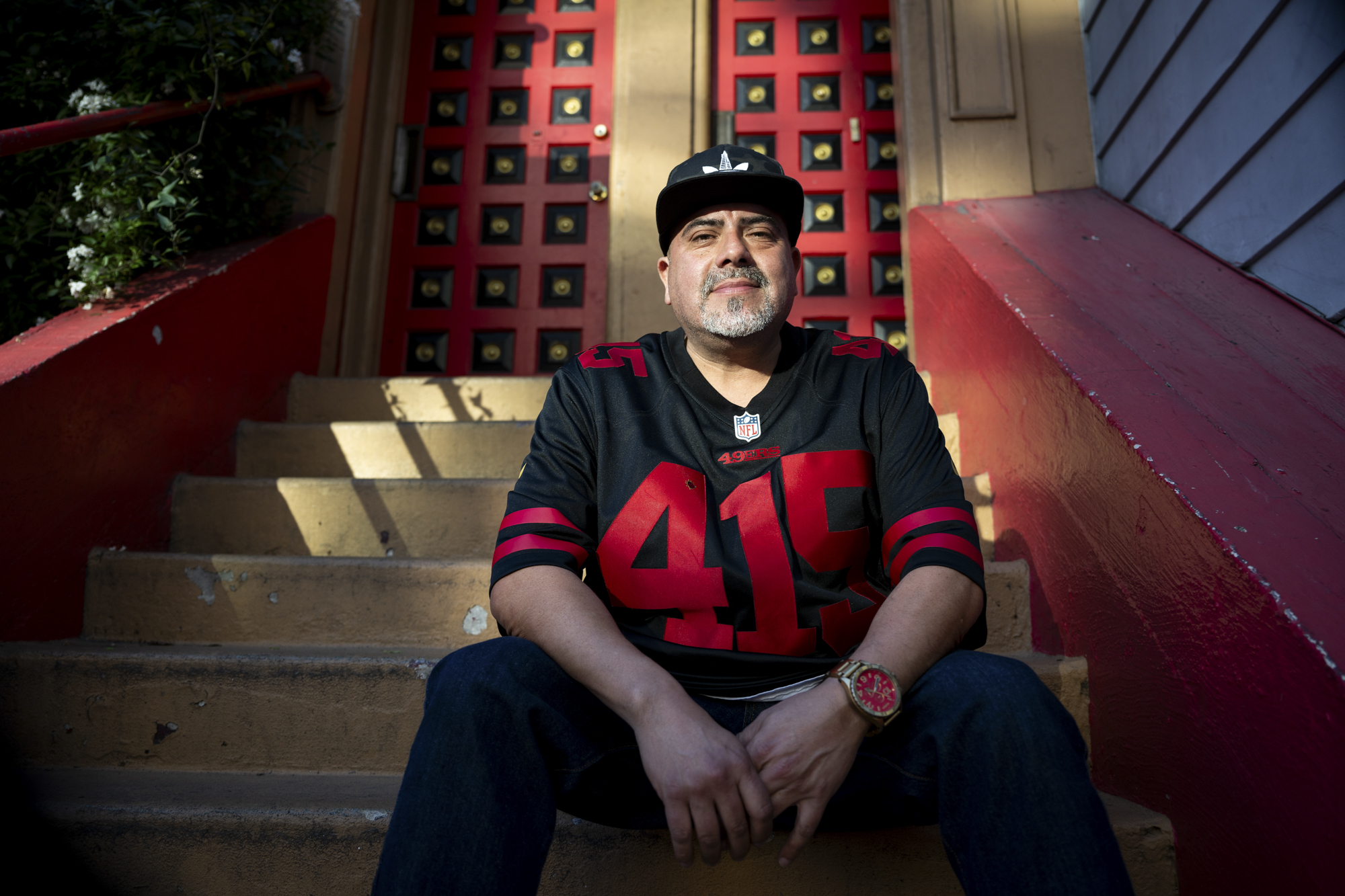 Man wearing a hat and football jersey sits on the stoop of a home