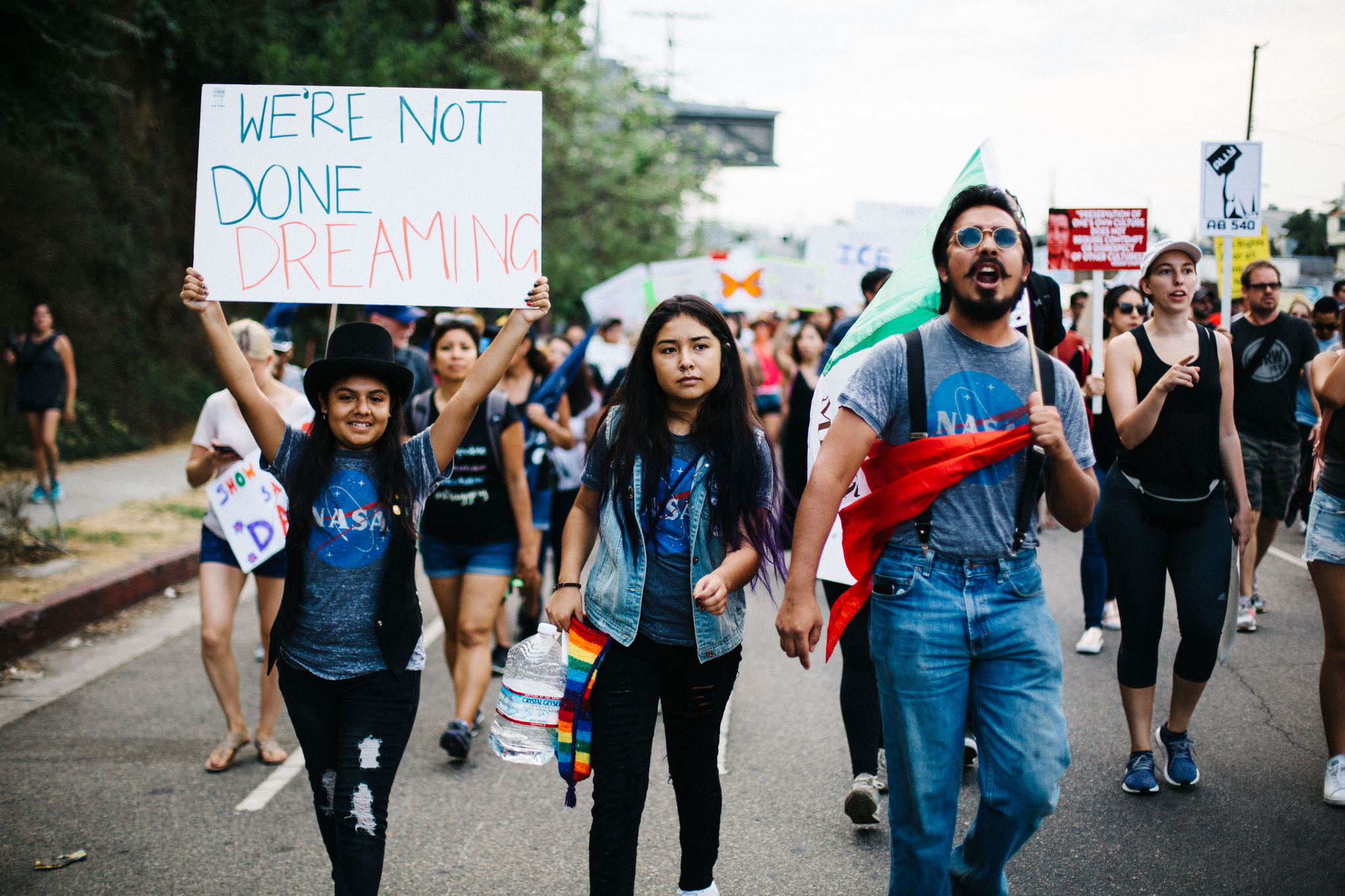 People protesting, including adults and children, with a young girl holding a sign that says "We're not done dreaming."