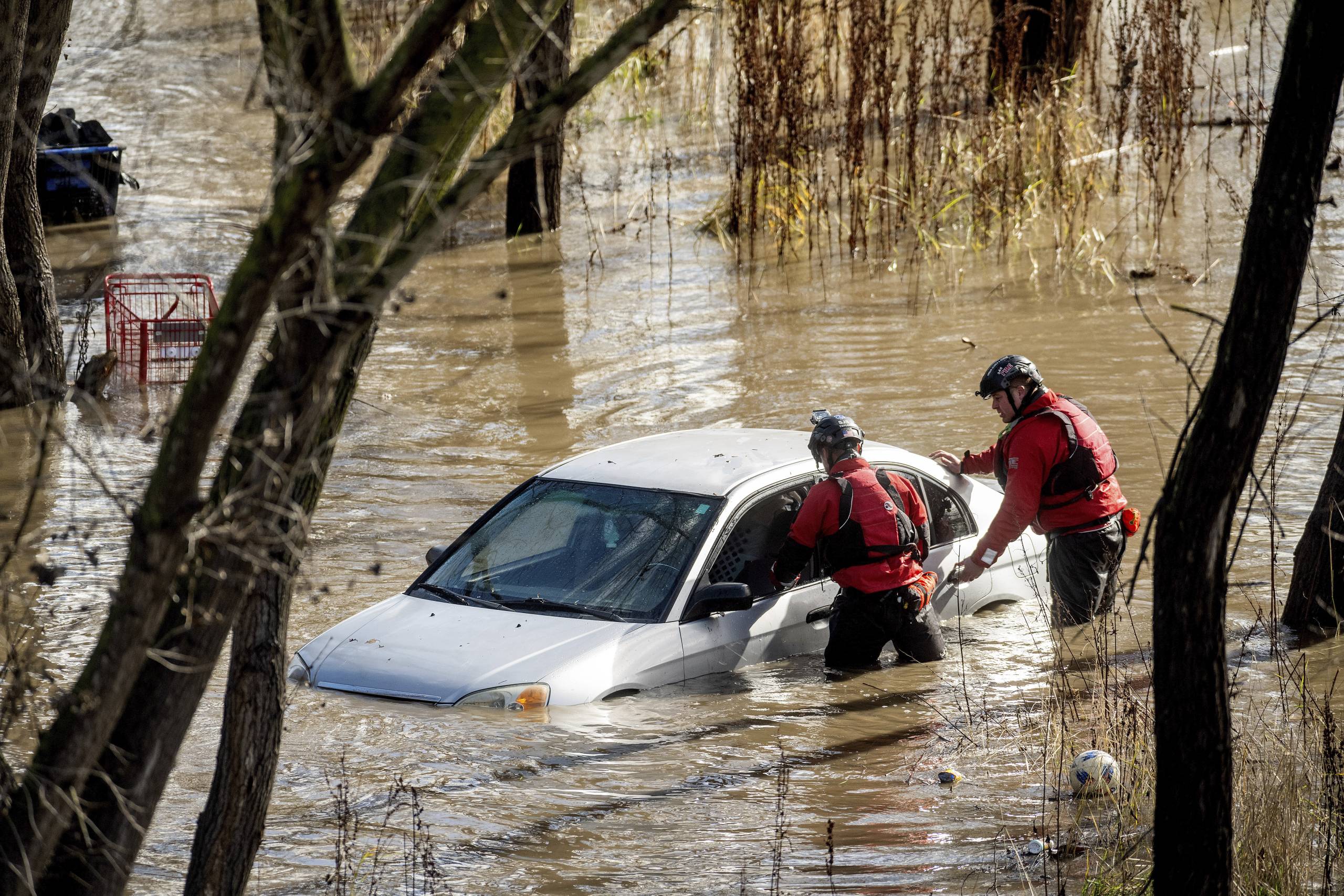 Search and rescue workers investigate a car surrounded by floodwater