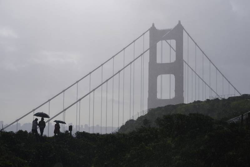 People walk in the rain as a storm moves through with the Golden Gate Bridge in the background