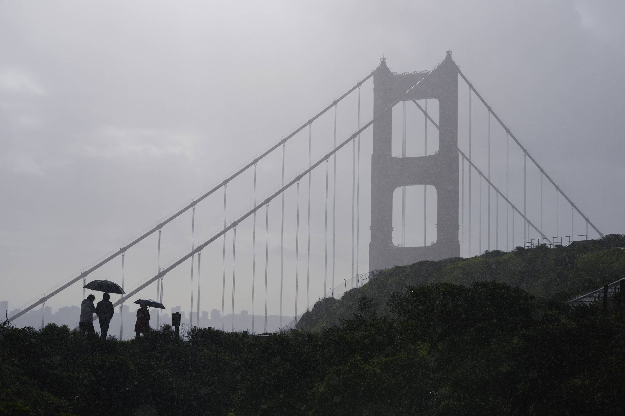 People walk in the rain as a storm moves through, with the Golden Gate Bridge in the background.
