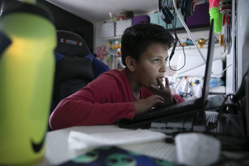 A boy staring at a computer screen during a remote learning session in his room.