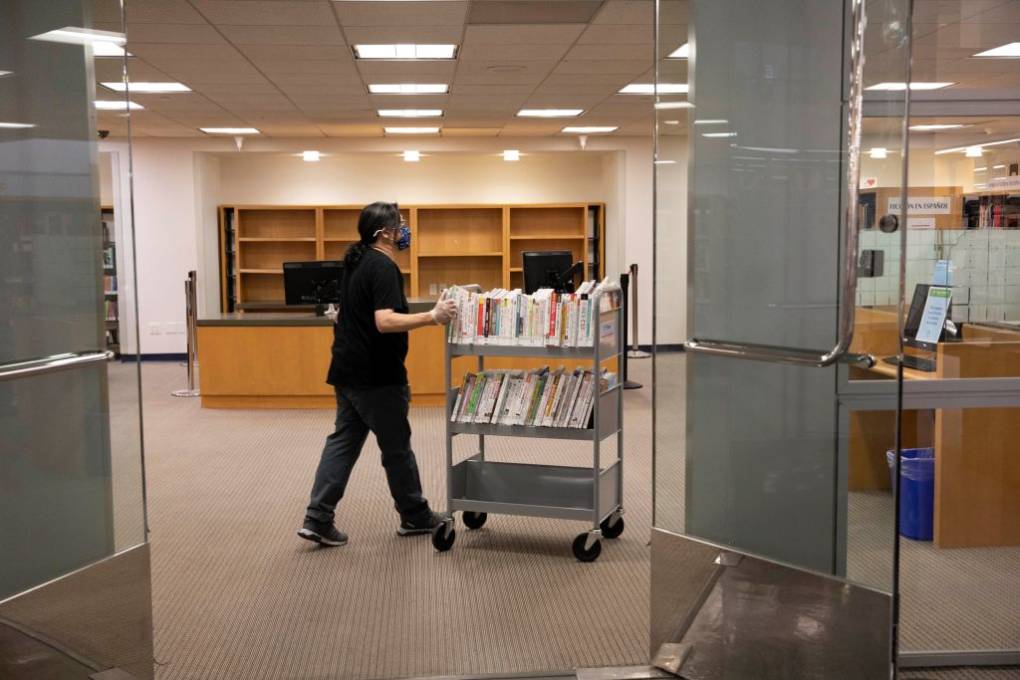 A woman pushes a book cart in a part of a library.