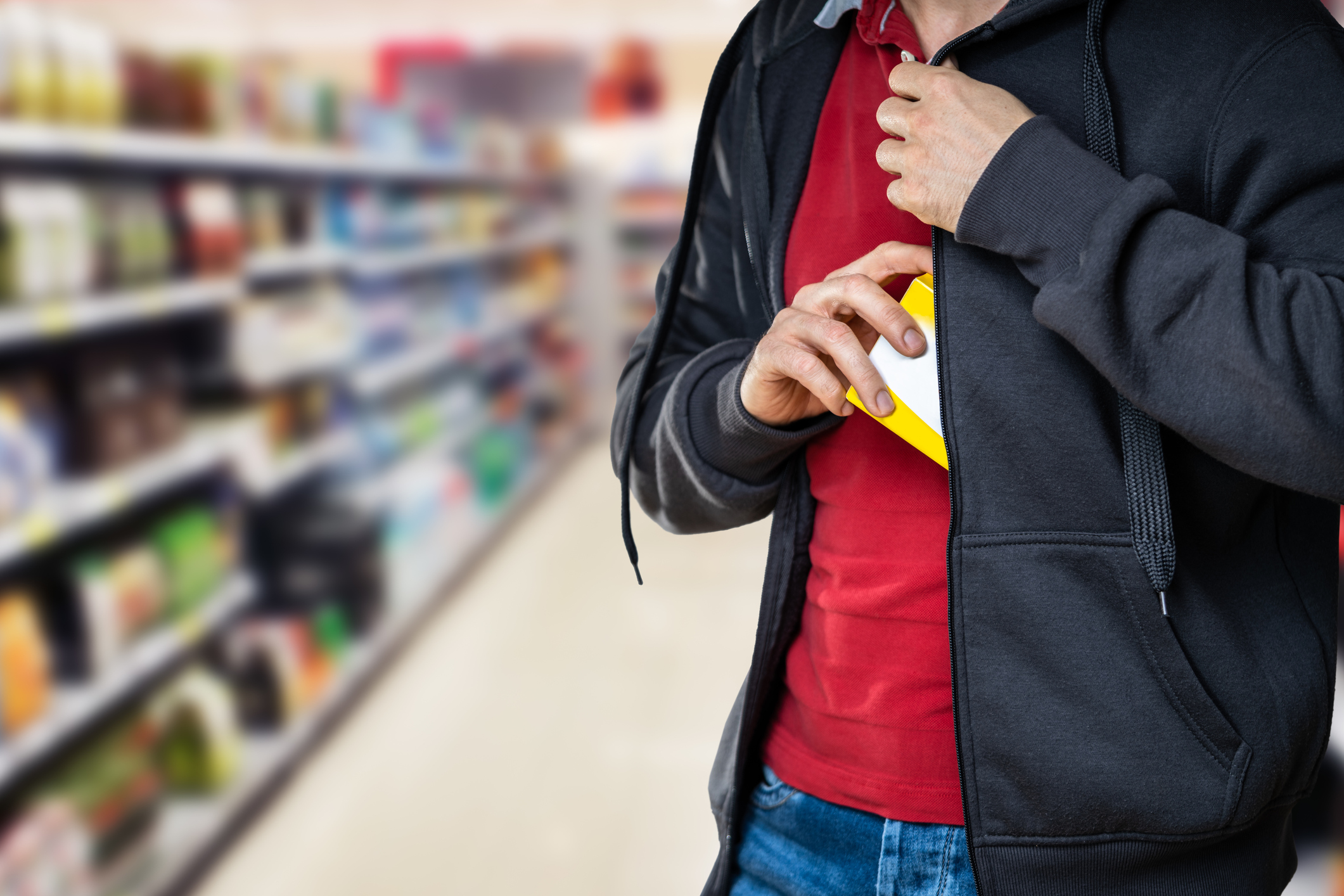 An image of a person putting an item into their jacket in a store.