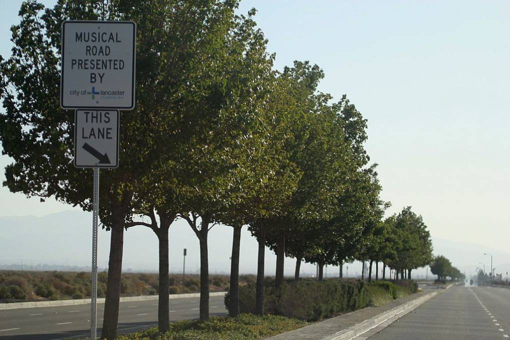 A stretch of road with trees lined up on one side and a sign that reads "Musical Road Presented by city of Lancaster."