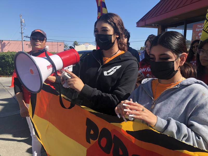 Two young women with a sign and one holding a megaphone, both are masked.