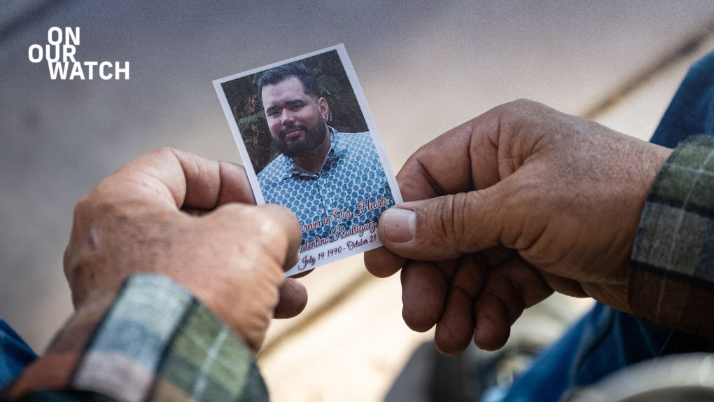 A man's hands hold a small photo of a young latino man with a black beard wearing a blue patterned shirt.