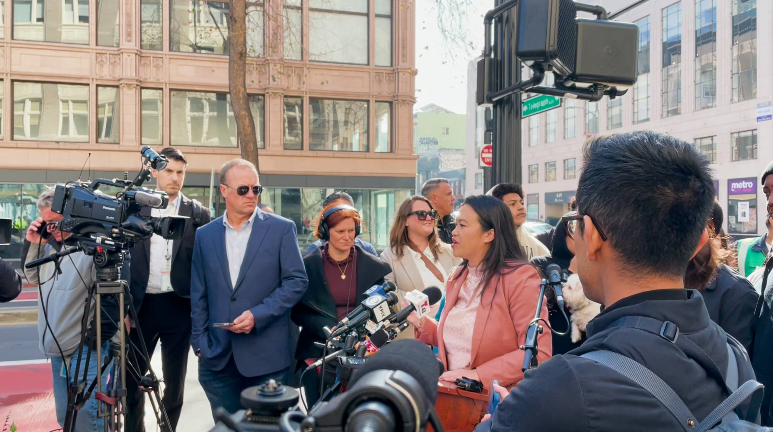 An Asian woman speaks at a press conference on the street as people surround her.