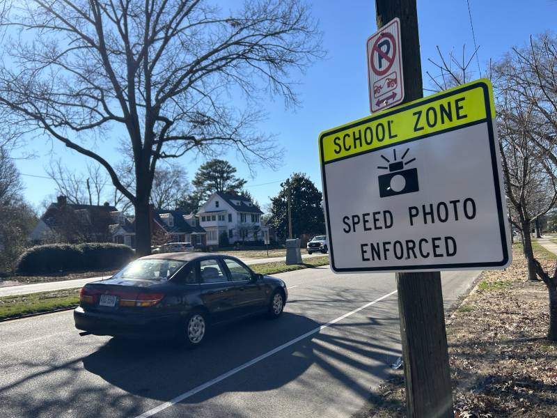 A car drives past a sign that says, 'school zone: speed photo enforced.'