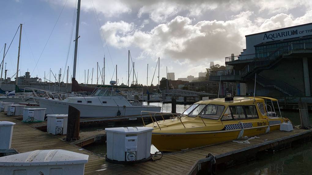 A yellow boat taxi is pulled up to a dock with other boats and a dramatic sky in the background.