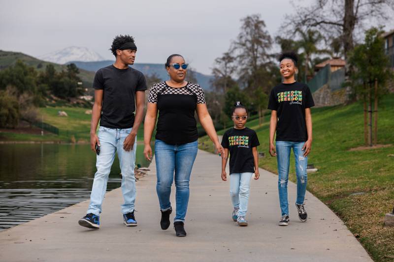 A young Black man, an adult Black woman and two young Black girls walk down a path.