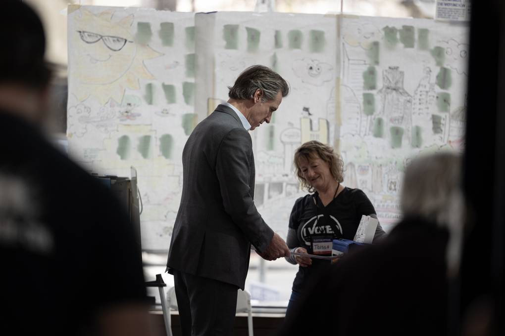 A man wearing a suit stands hands a woman in a t shirt that says "I Voted" a piece of paper.