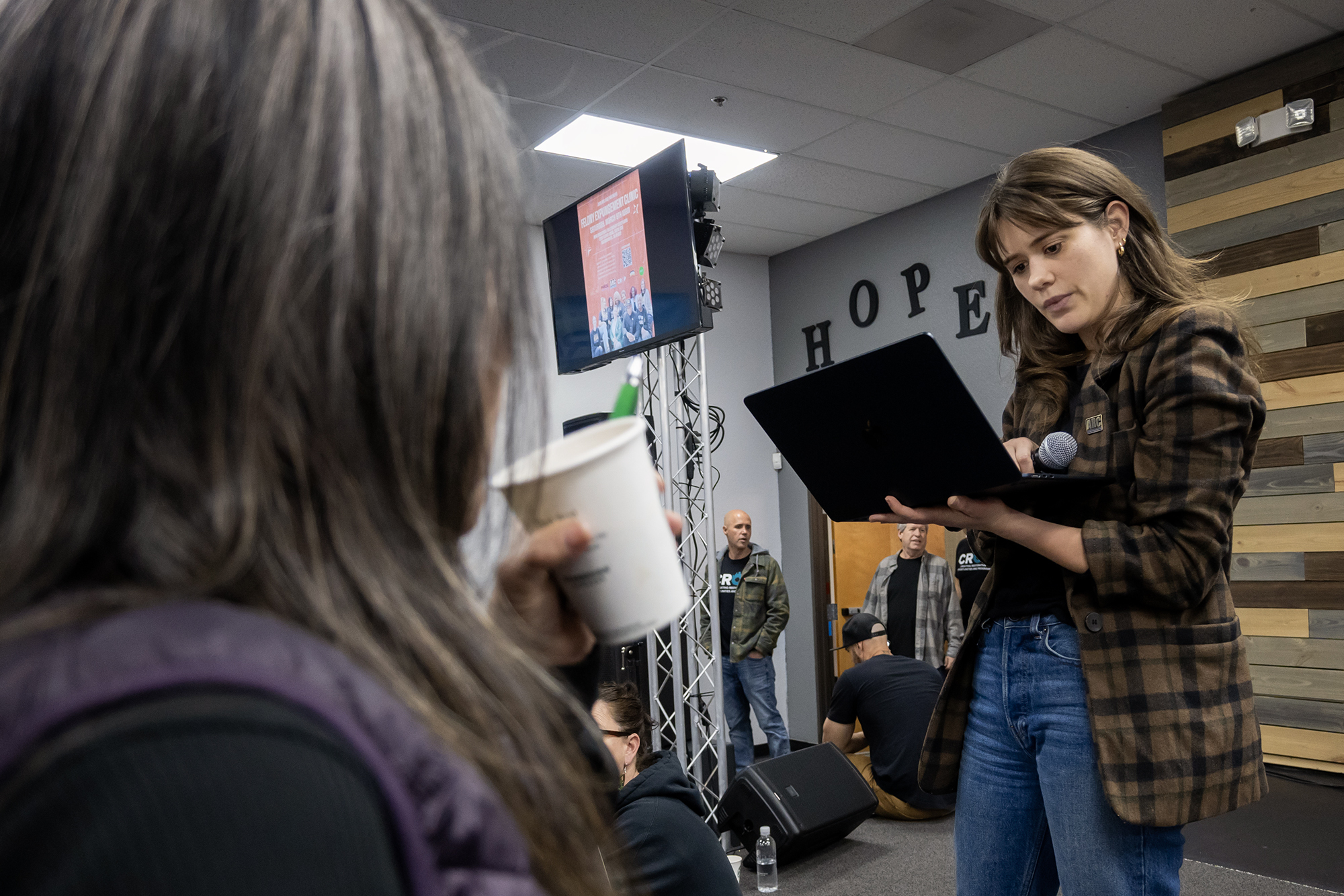 A woman looks at a laptop in her hand in front of a group of people.
