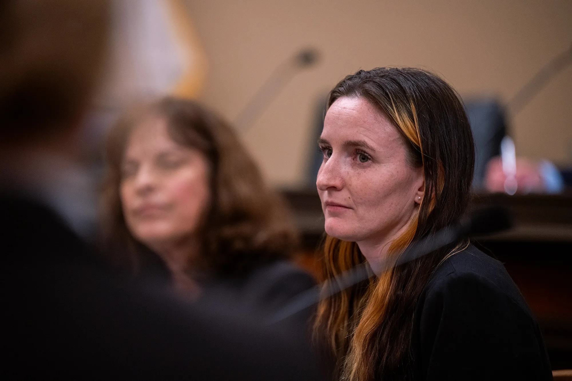 A concerned-looking white woman looks on in a courtroom with another woman in the background.