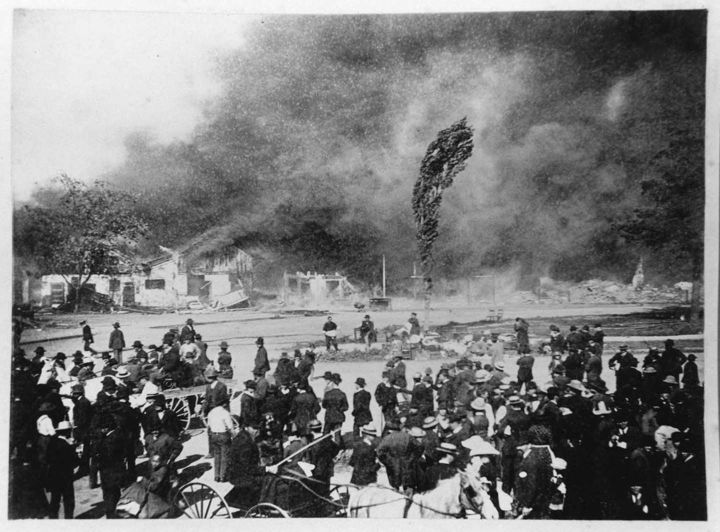 A black and white photo with a blazing city and people watching in the foreground.