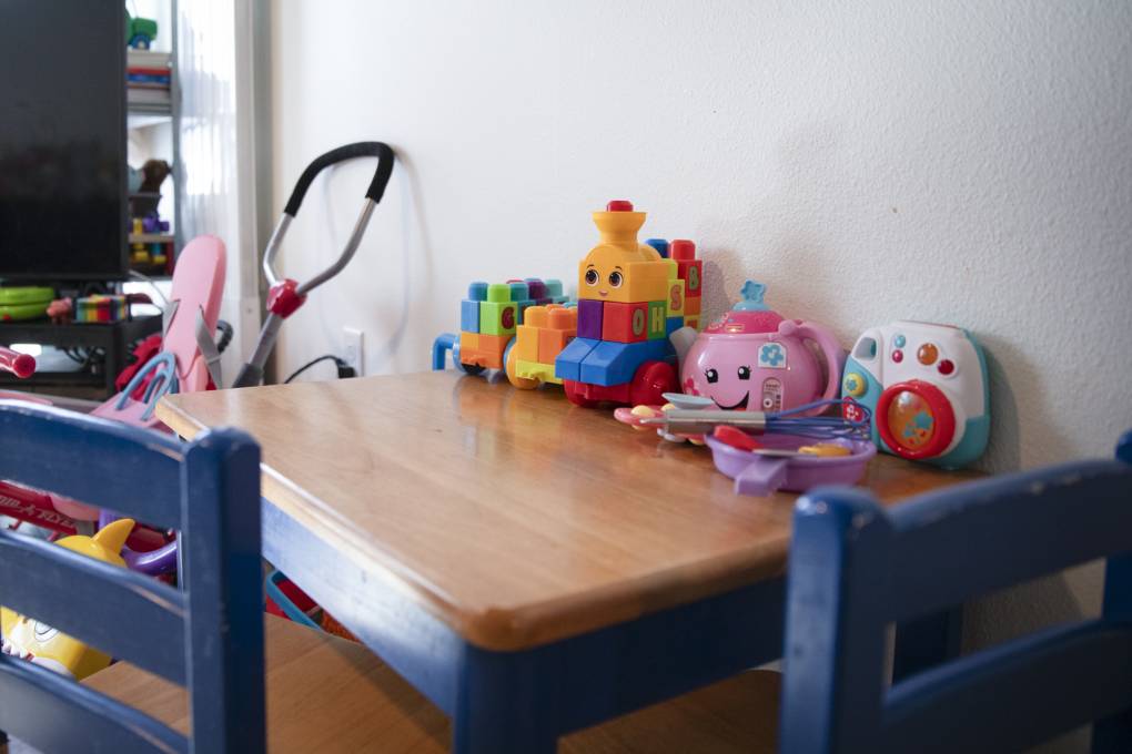 A collection of kids' toys sits on a beige and blue table beside a white wall.