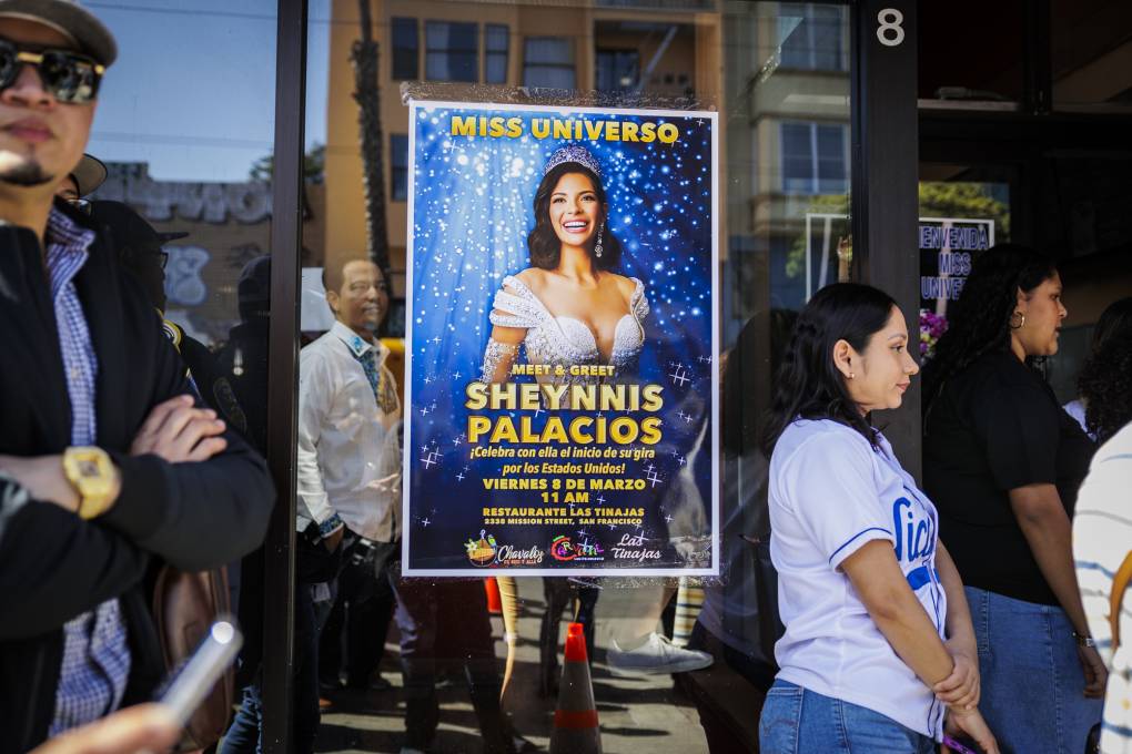 People stand around a poster depicting a Miss Universe winner, Sheynnis Palacios.