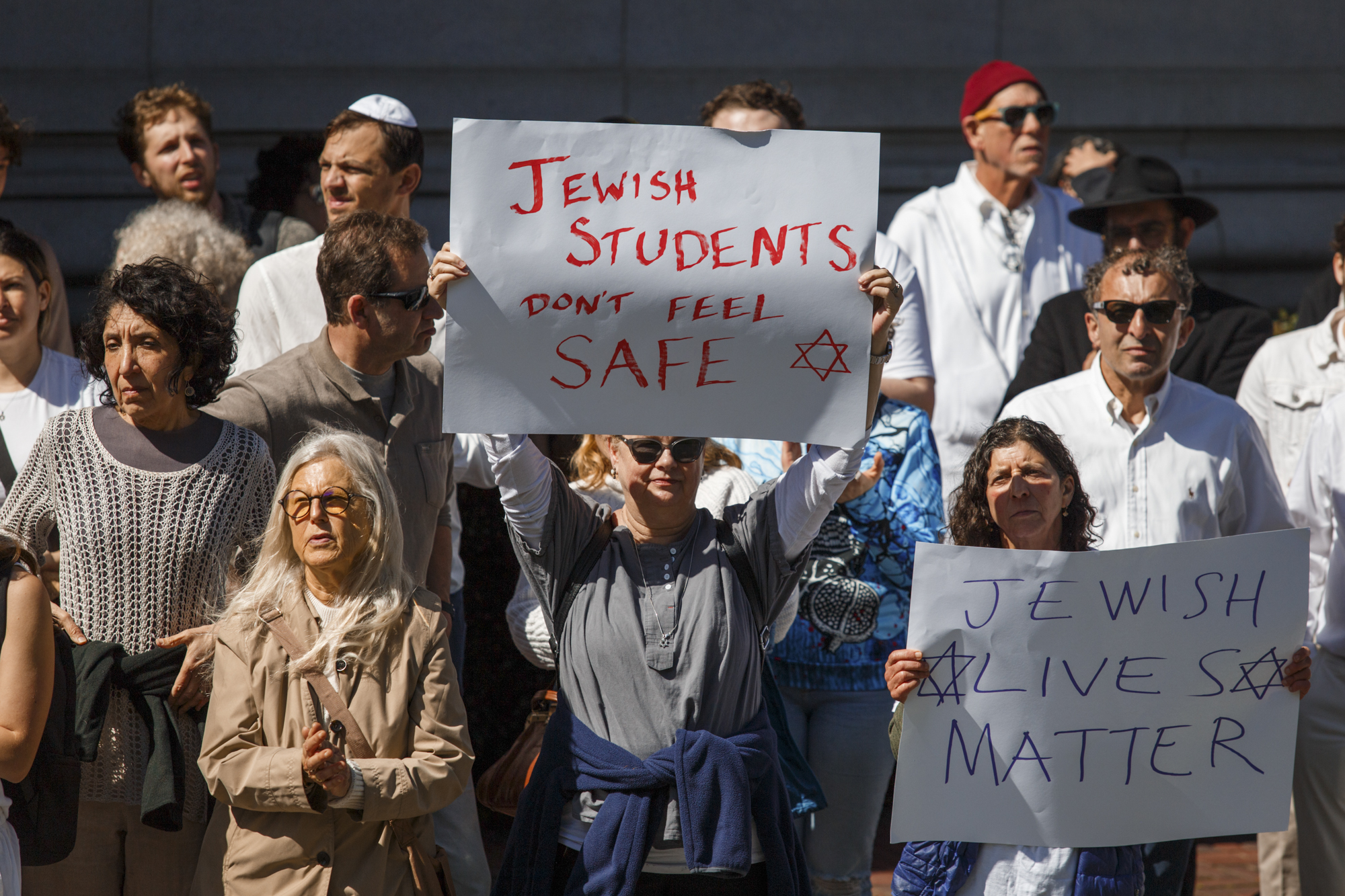 A large group of people stands together, holding signs.