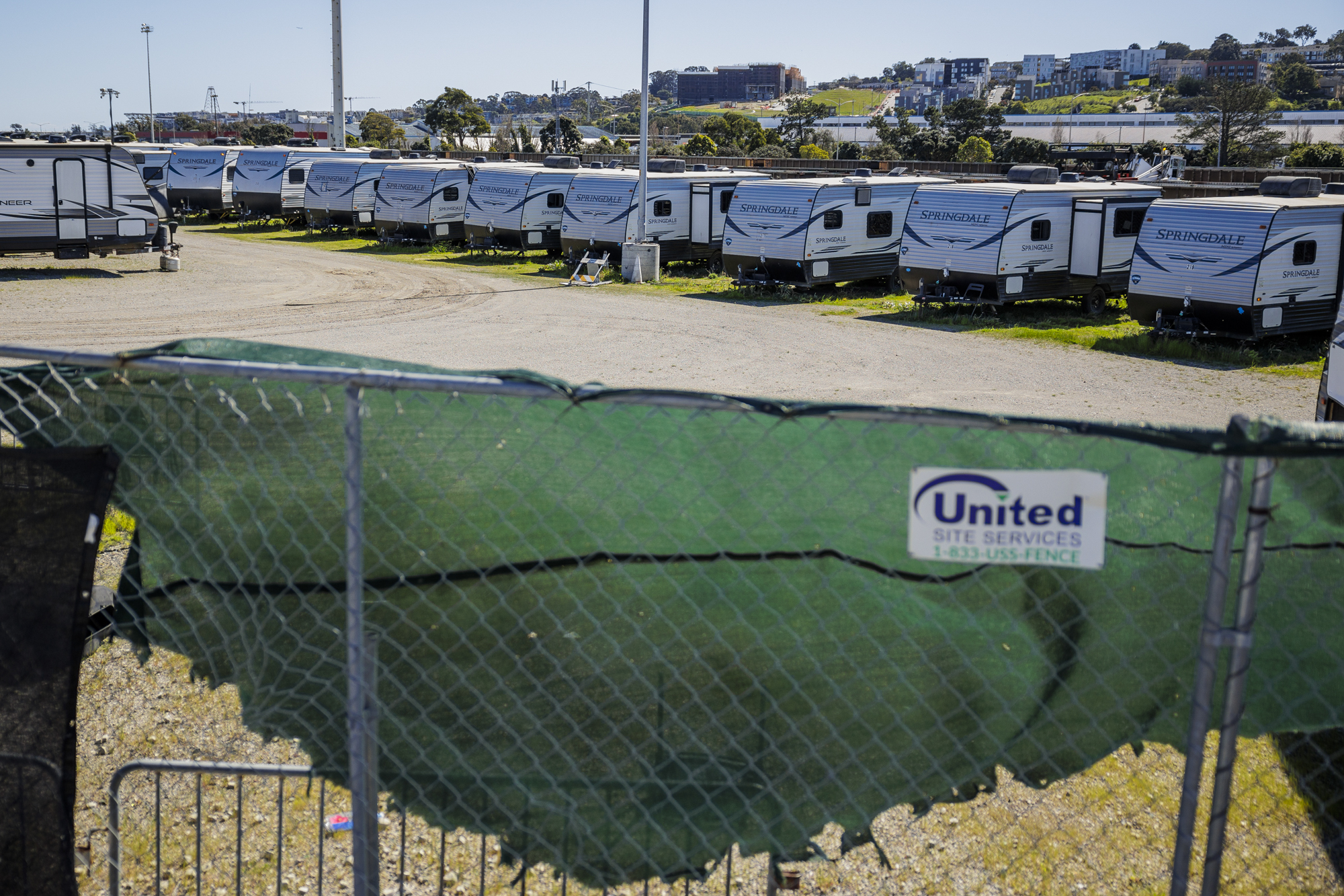 A line of trailers sits inside a park with wire fencing in the foreground.