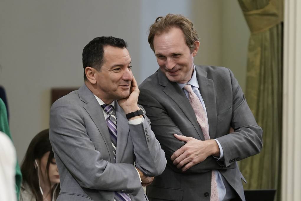 Two men in light gray suits talk and share a laugh.