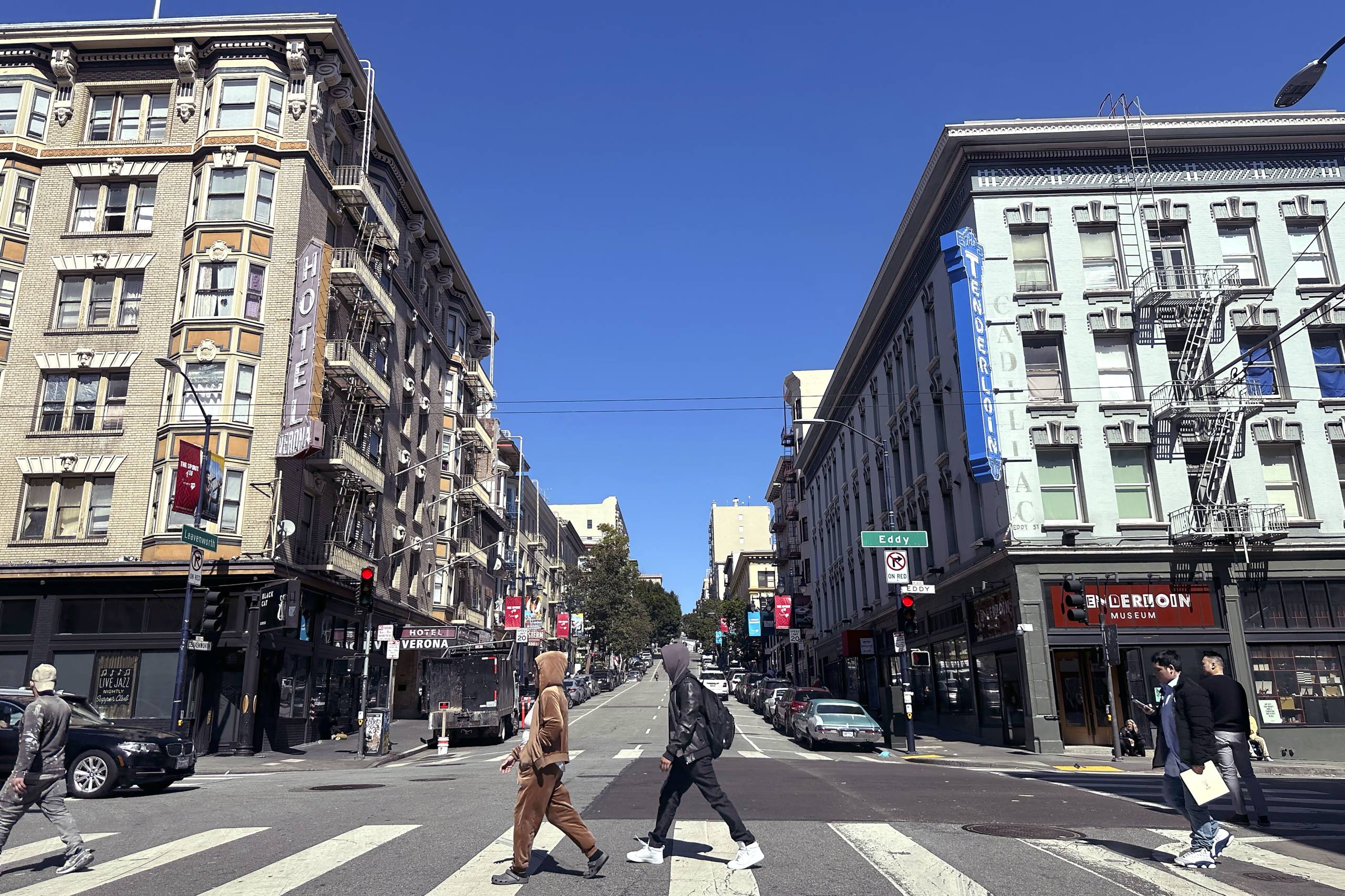 A view of a city street with people walking across an intersection.