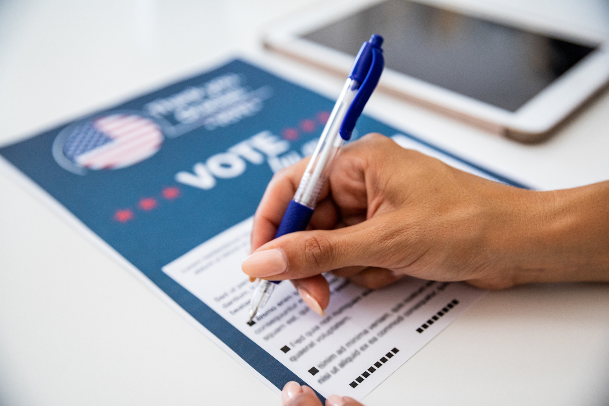 A hand of a woman holding a pen and filling out a voting form.