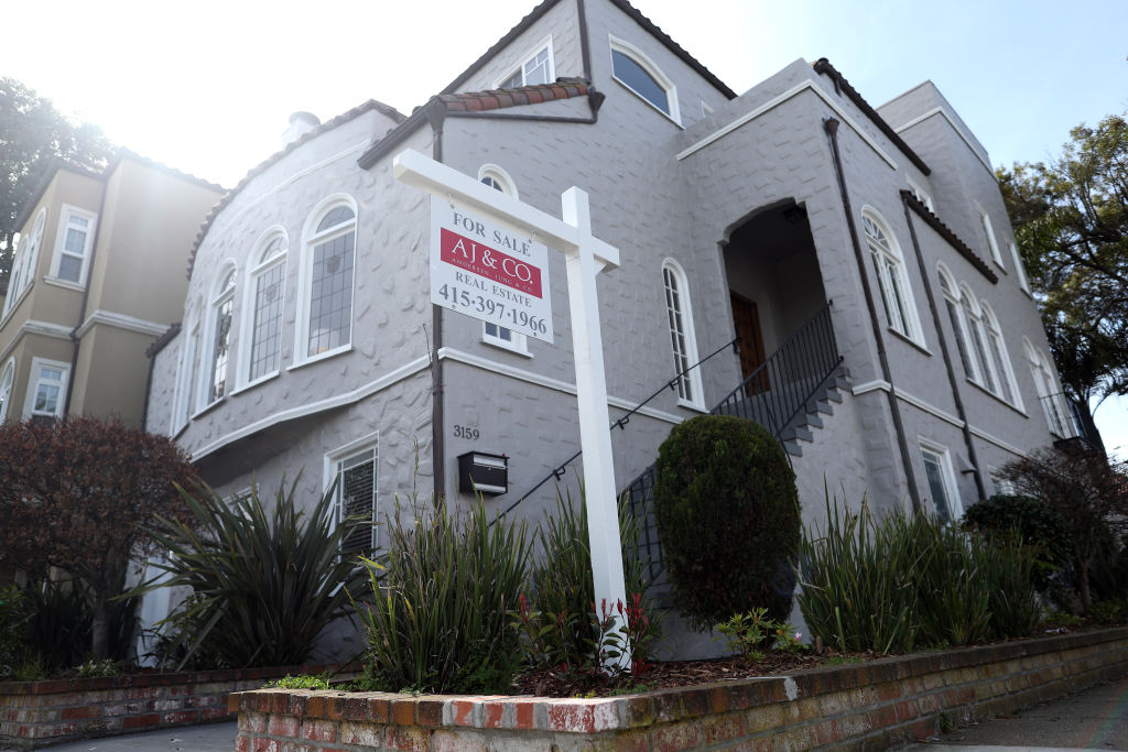 A 'For Sale' sing in front of a grey single-family house.