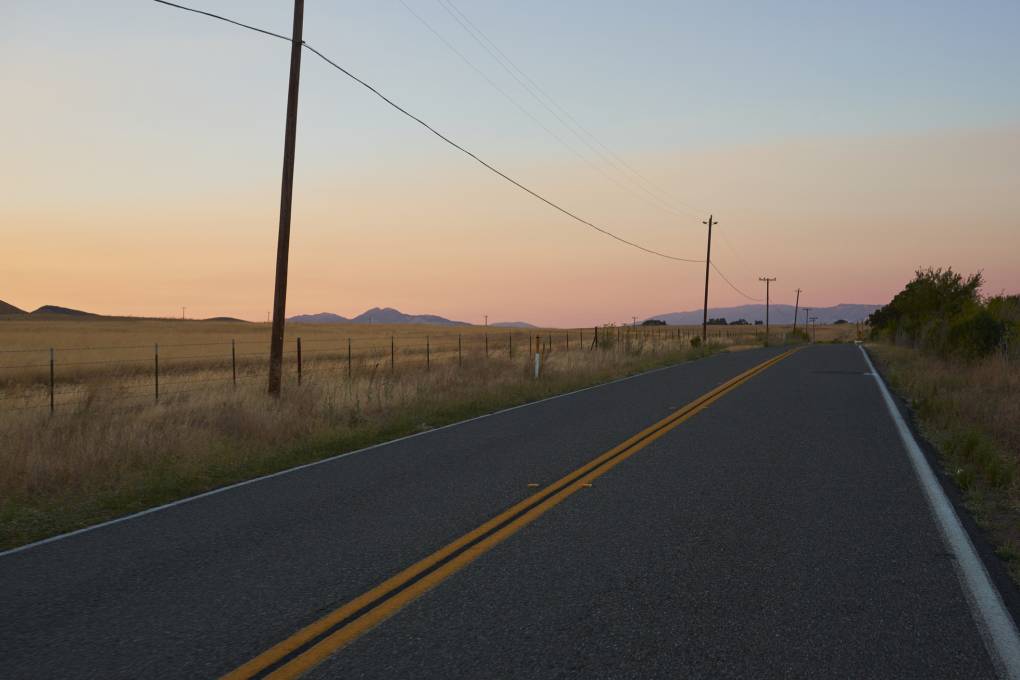 Telephone line runs along a rural two-lane highway at sunset.