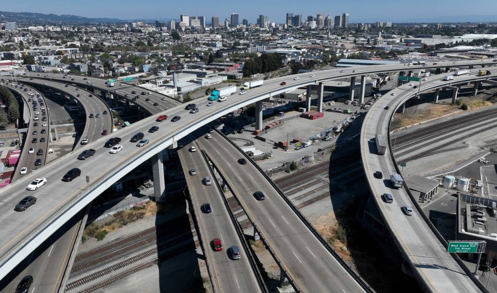 Crisscrossing freeways are seen from above, with the city of Oakland in the background.