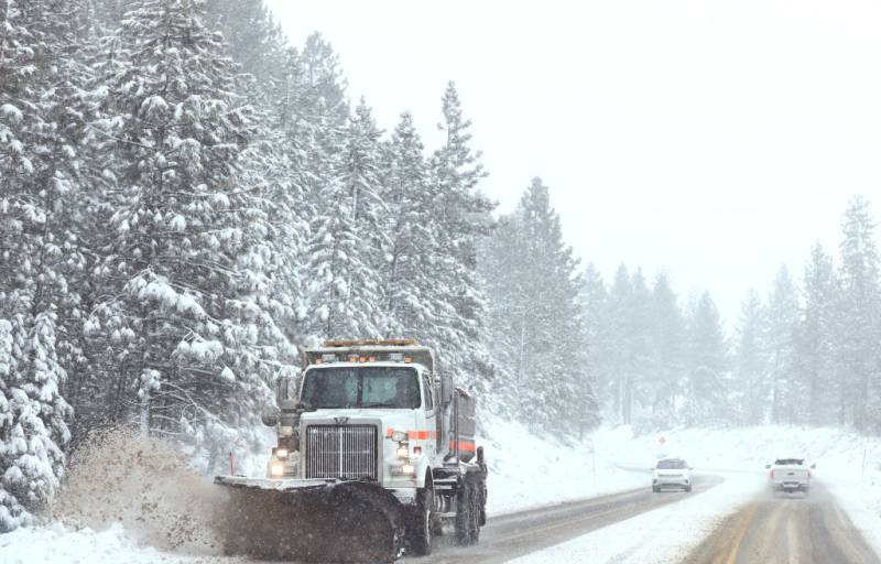 A snowplow clears snow as a car approaches on a snow-covered highway.