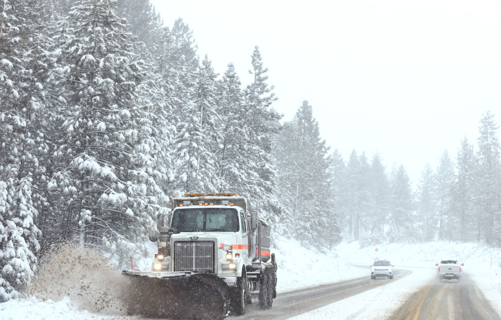 A snowplow clears snow as a car approaches on a snow covered highway.