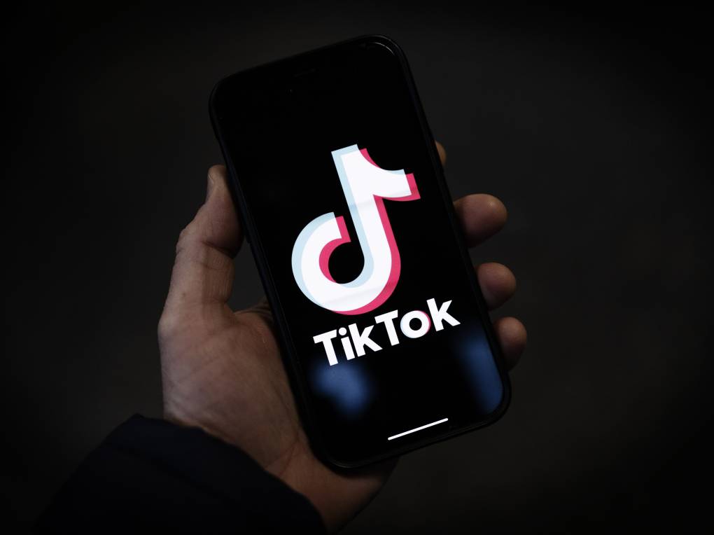 A hand holds a smartphone with a large logo that reads "Tik Tok."