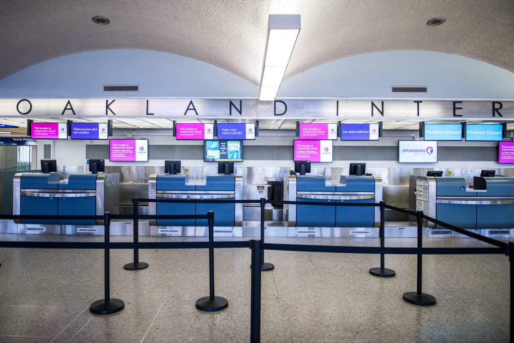 An airport terminal with line dividers and luggage check with a sign that reads "Oakland International."