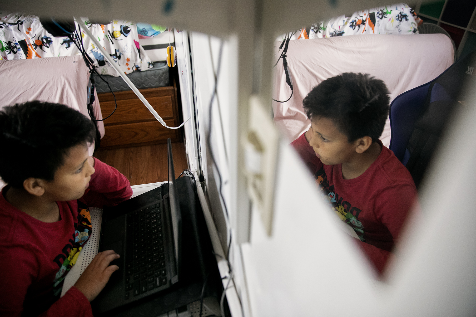 An image is seen from a mirror as a child sits down and looks at a laptop.