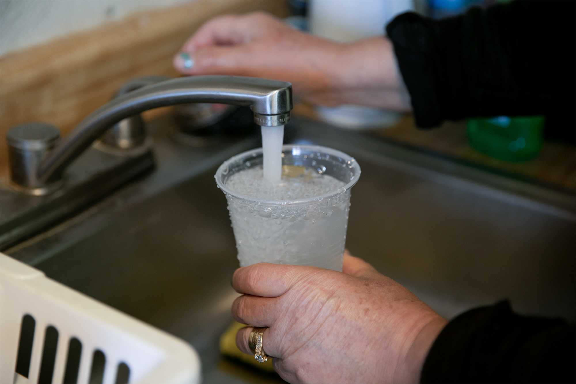 A hand holds a cup as the other turns the knob of a faucet to fill the cup with water.