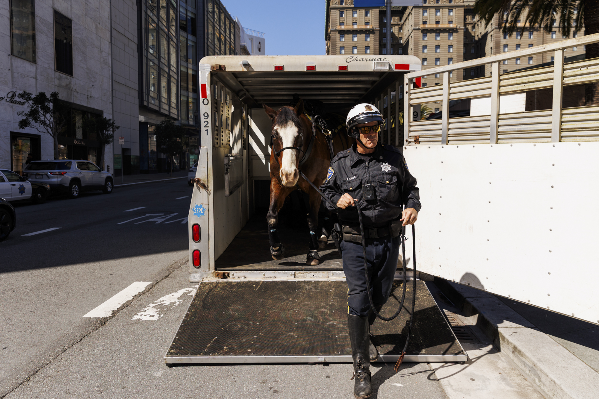 A police officer in uniform leads a horse out of a trailer in downtown San Francisco.