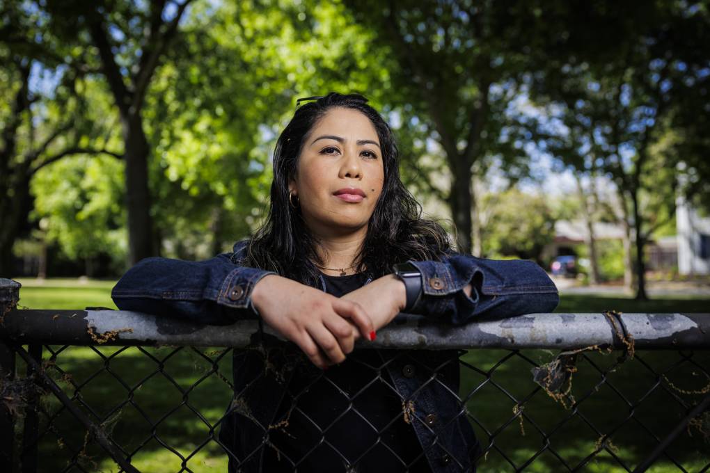 A Latino woman leans against a fence.