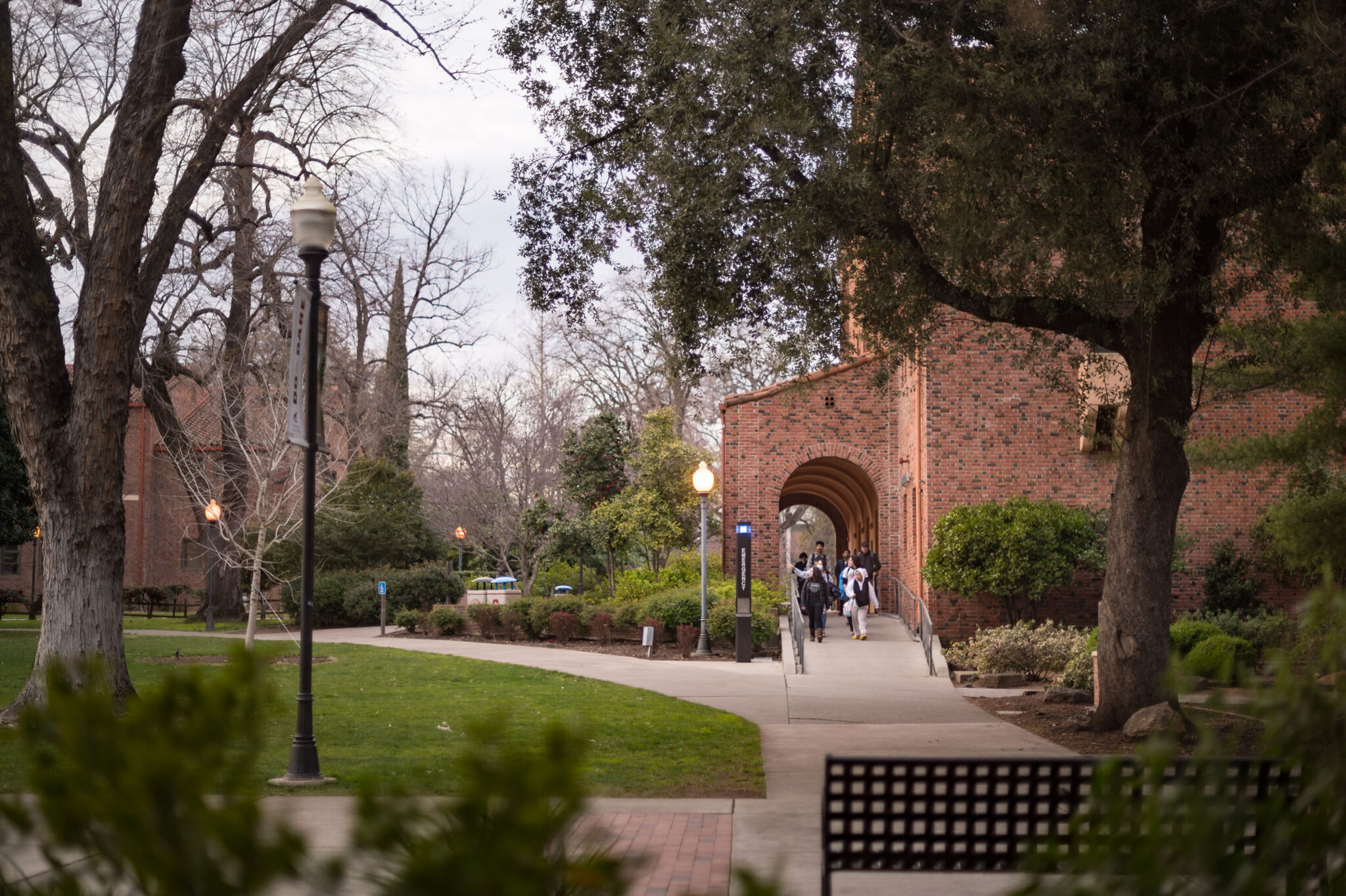 A group of people walk out of a building on a college campus.