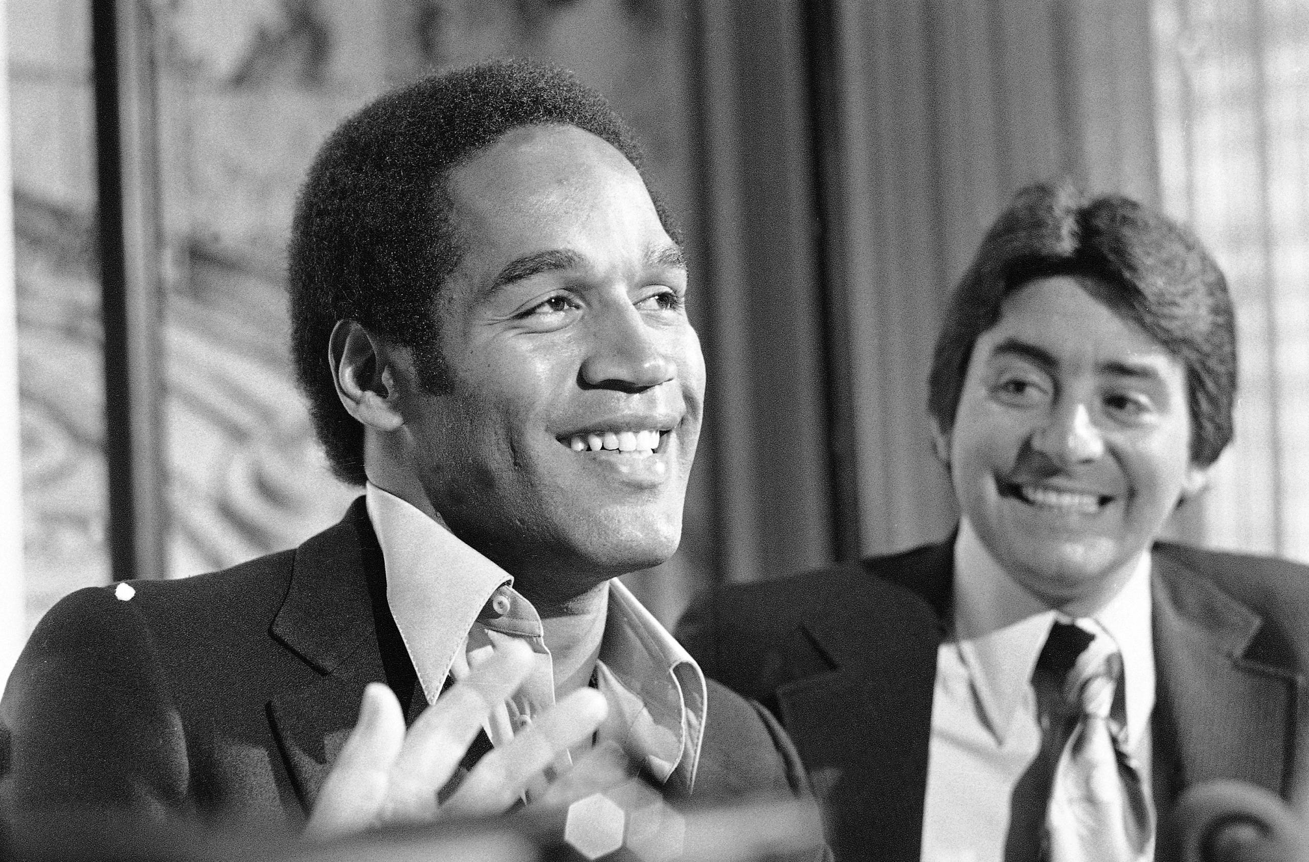 A black and white image of a Black man smiling wearing a business suit next to a white man with glasses in a business suit.