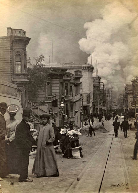 Black and white photo of early San Francisco. A small group of African Americans turn to the camera as huge smoke plumes rise behind them.