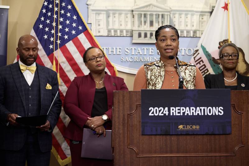 A woman stands at a podium with an American flag behind her.