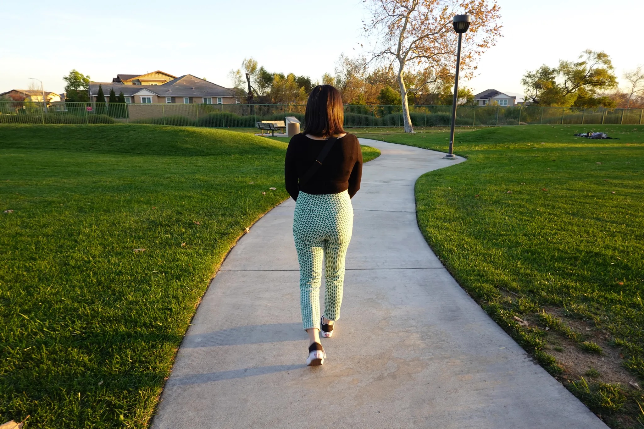 A young woman seen walking along a path surrounded by lawns on a campus.
