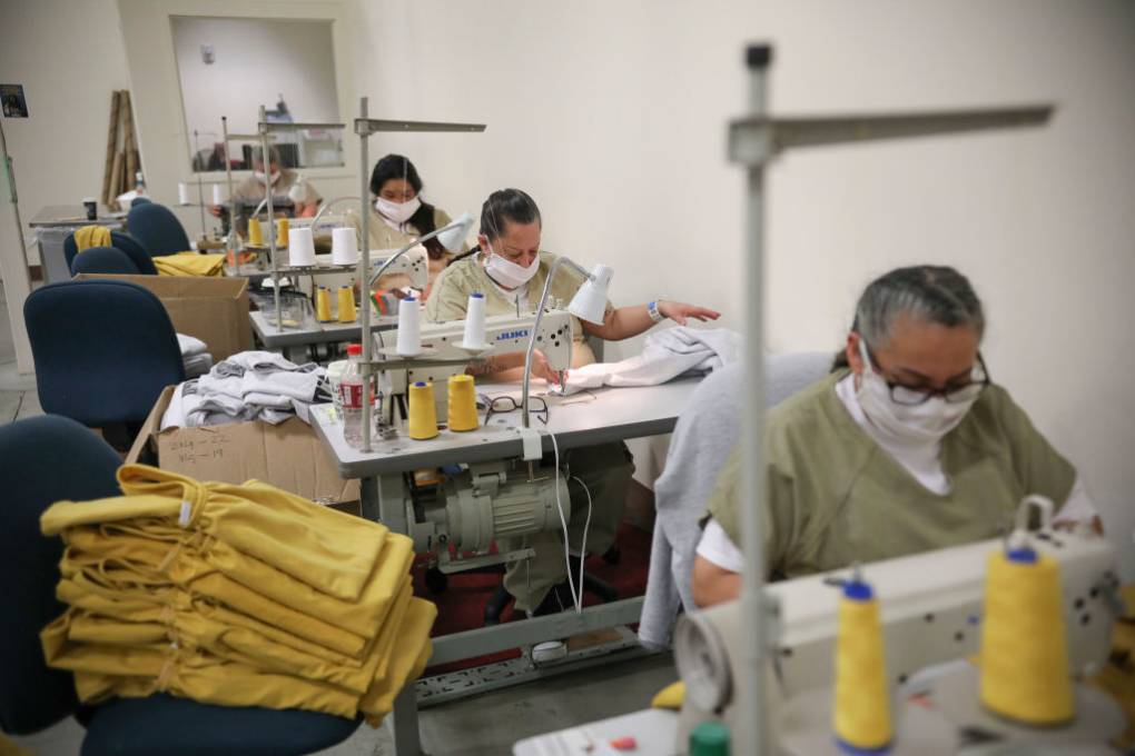 Incarcerated women in beige outfits work at sewing tables.