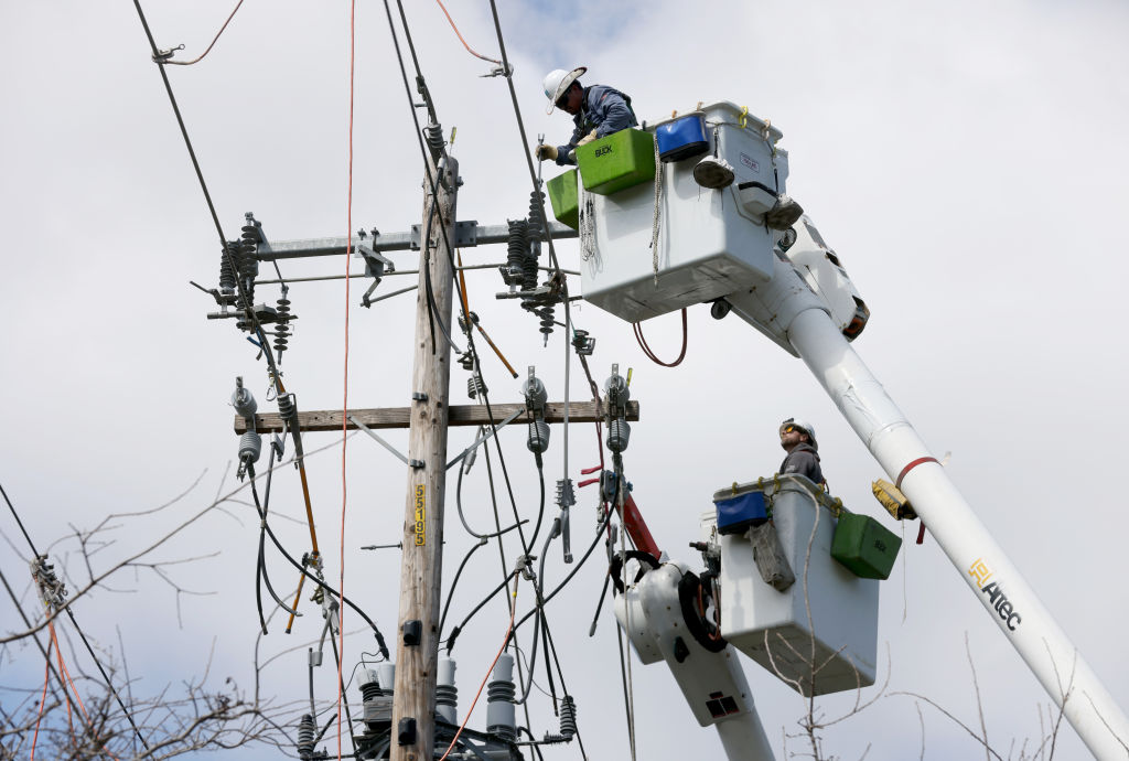 Two electrical workers on a cherry picker make repairs to a powerline.