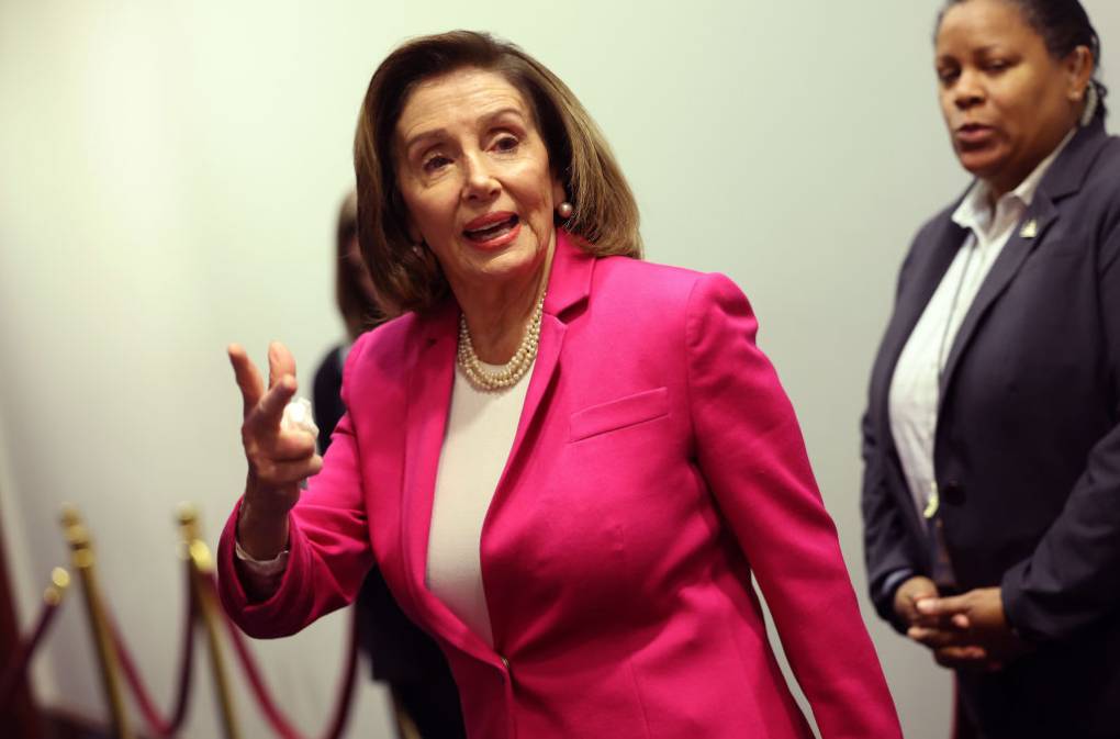 An older woman in a pink suit gestures toward the camera.