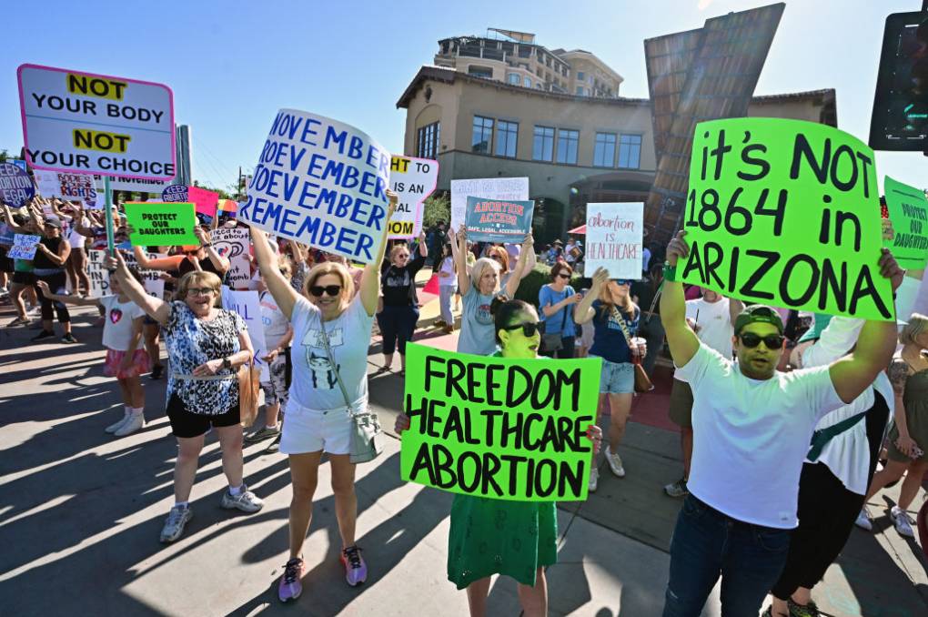 Pro-choice protesters stand on a street holding up signs in support of abortion rights, including one that says: 'It's not 1864 Arizona.'