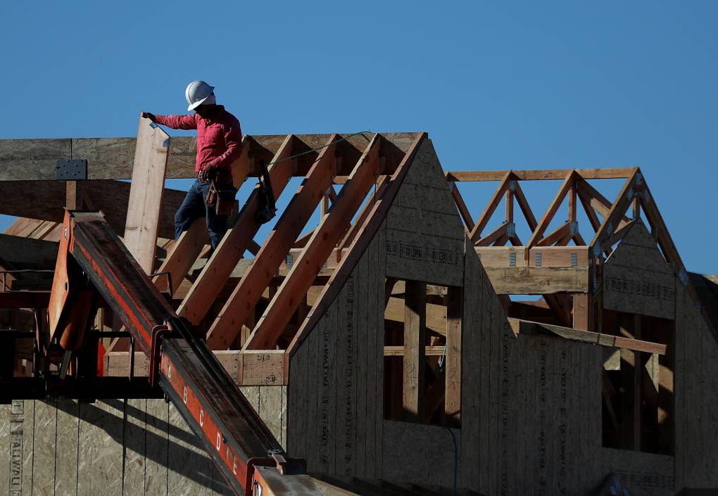 A person wearing construction equipment holds a wooden support beam while a roof is built.